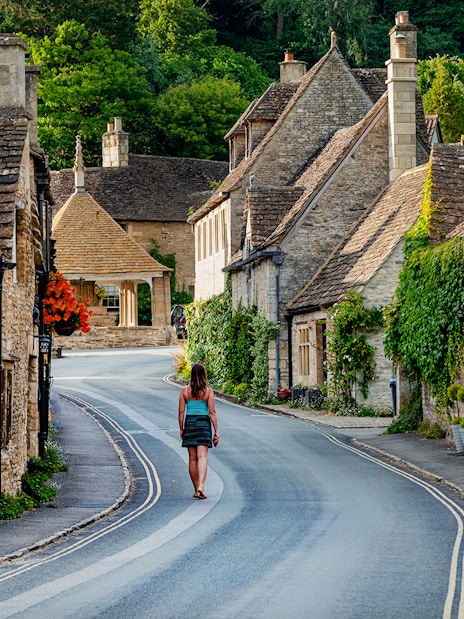 Tourist walking through a picturesque village street in the Cotswolds, England.