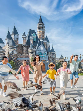 Visitors enjoying VinWonders Theme Park with castle backdrop and pigeons.