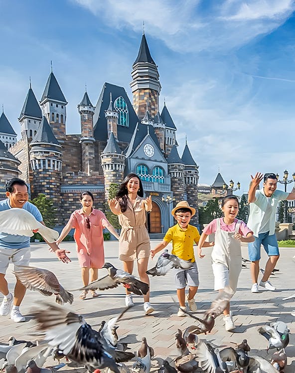 Visitors enjoying VinWonders Theme Park with castle backdrop and pigeons.