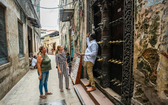 Tour guide explaining ornate door to visitors in Stone Town, Zanzibar.