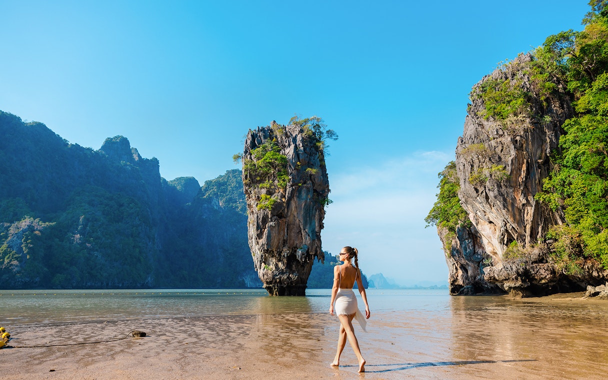 Tourist walking on a beach near limestone cliffs in Phang Nga Bay, Thailand.