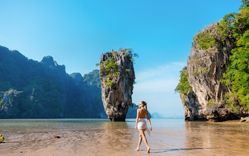 Tourist walking on a beach near limestone cliffs in Phang Nga Bay, Thailand.