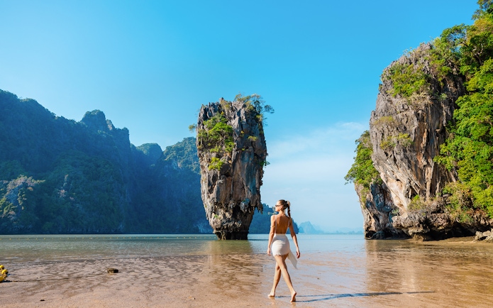 Tourist walking on a beach near limestone cliffs in Phang Nga Bay, Thailand.
