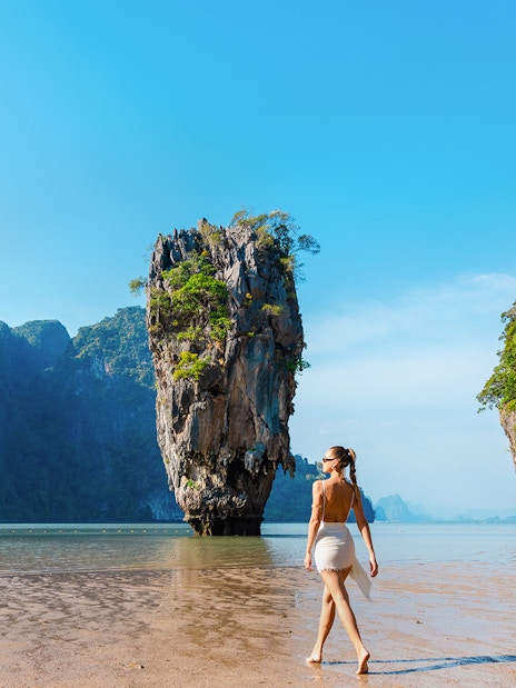 Tourist walking on a beach near limestone cliffs in Phang Nga Bay, Thailand.
