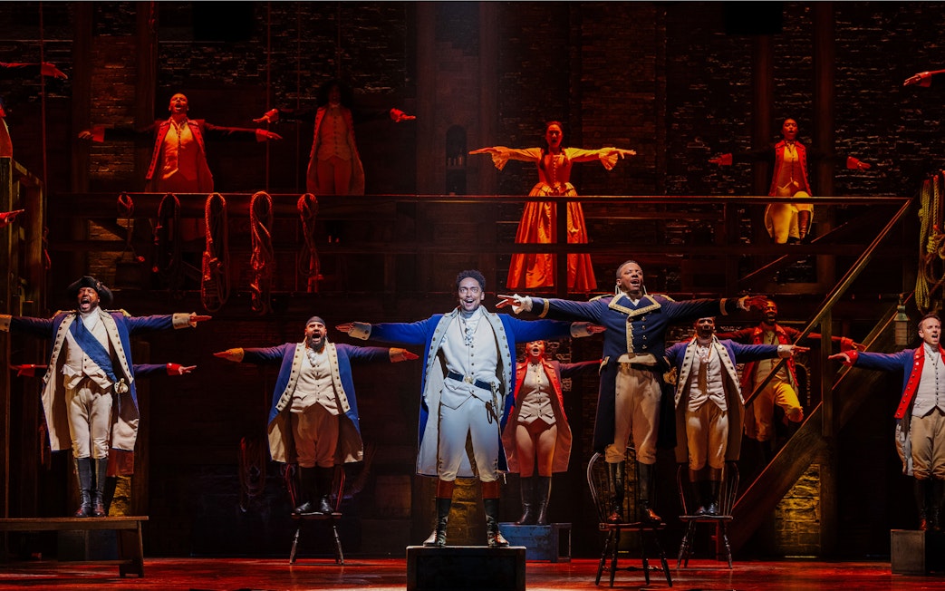 Actors performing a musical number in Hamilton production on stage.