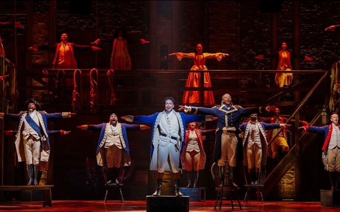 Actors performing a musical number in Hamilton production on stage.