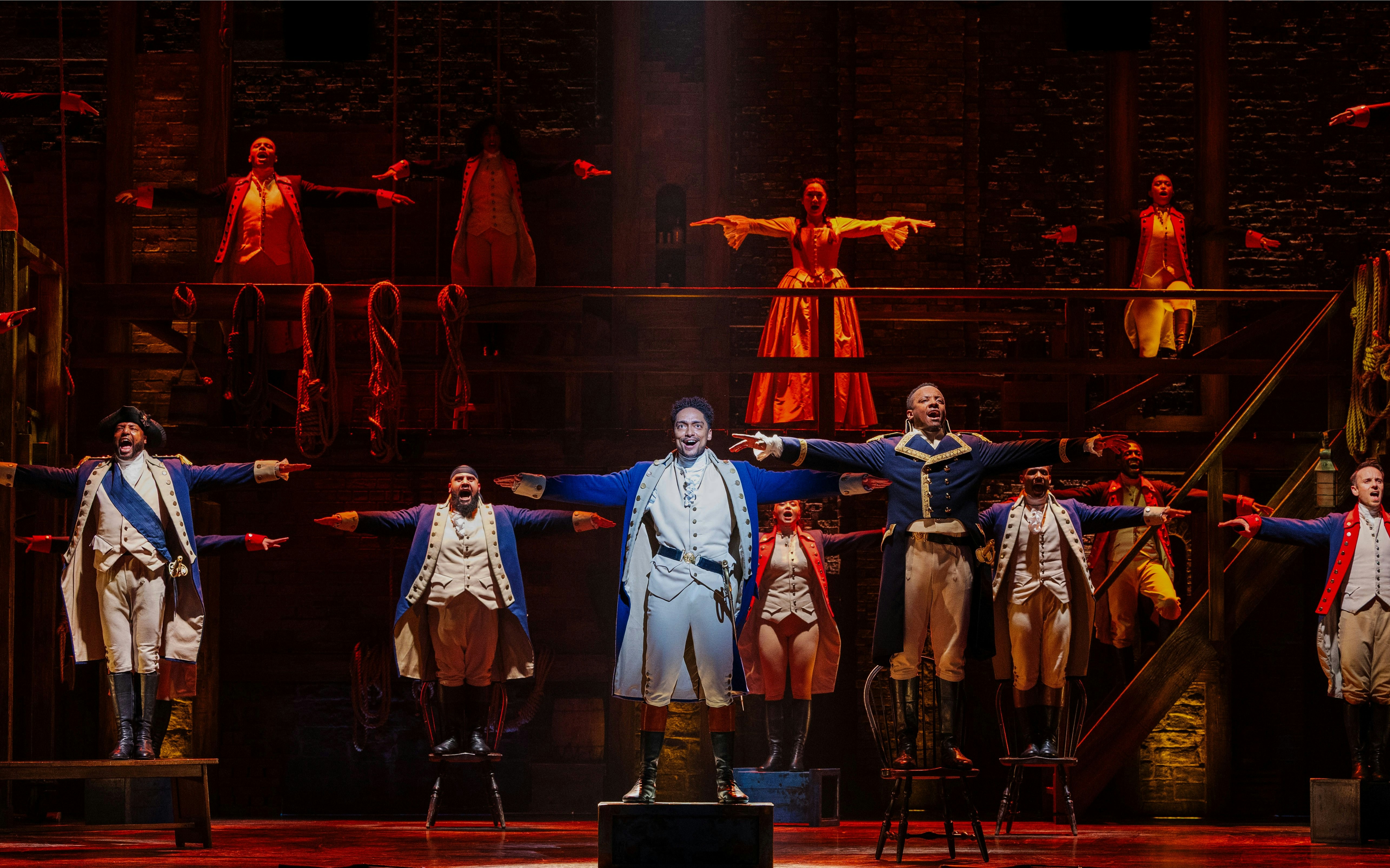 Actors performing a musical number in Hamilton production on stage.