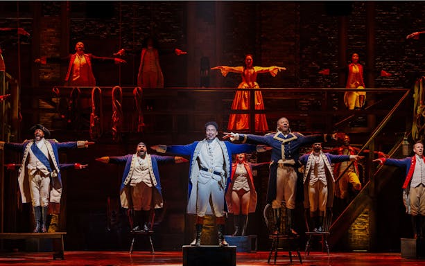 Actors performing a musical number in Hamilton production on stage.
