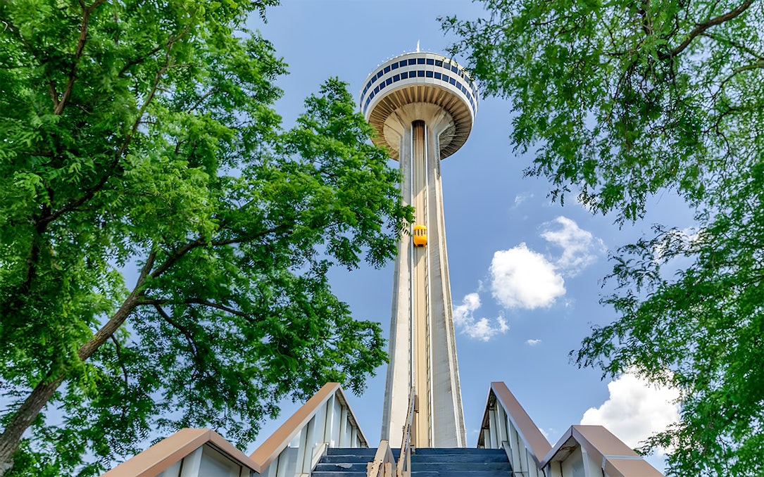 Skylon Tower viewed from below with surrounding trees and blue sky.