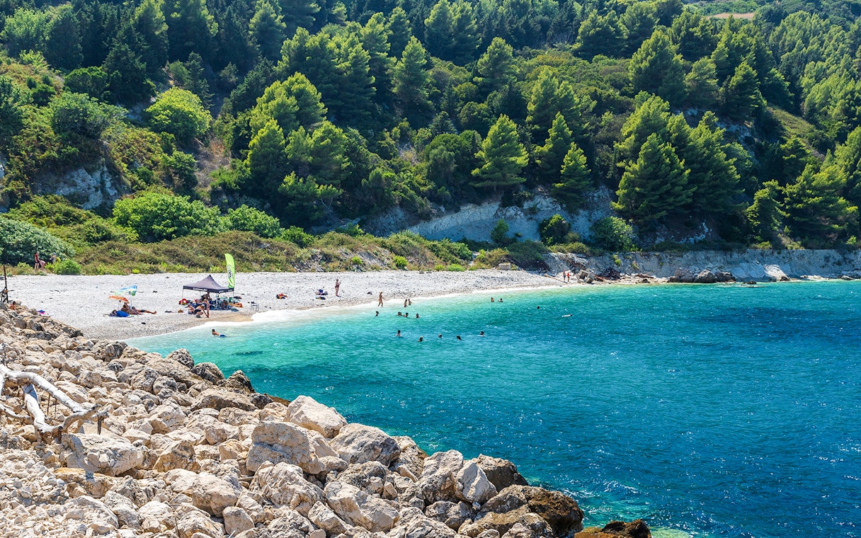 Beachgoers enjoying the clear waters and rocky shoreline of Sazan Island.