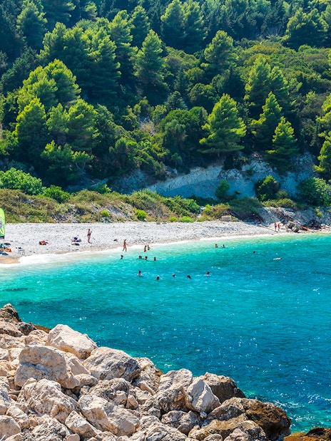Beachgoers enjoying the clear waters and rocky shoreline of Sazan Island.