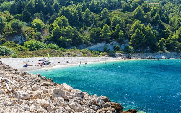 Beachgoers enjoying the clear waters and rocky shoreline of Sazan Island.