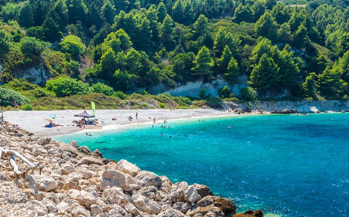 Beachgoers enjoying the clear waters and rocky shoreline of Sazan Island.