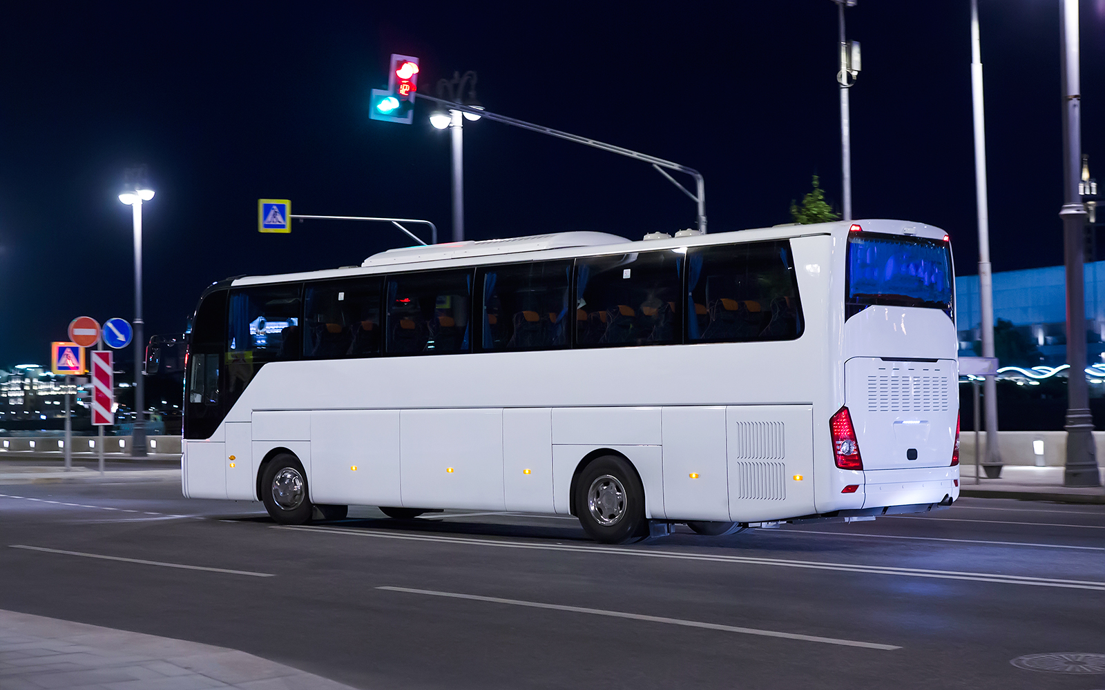 Tourist bus travels at night on city street under streetlights.