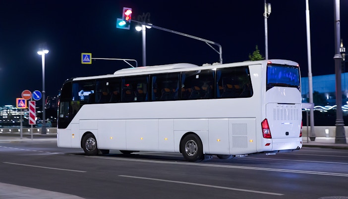 Tourist bus travels at night on city street under streetlights.