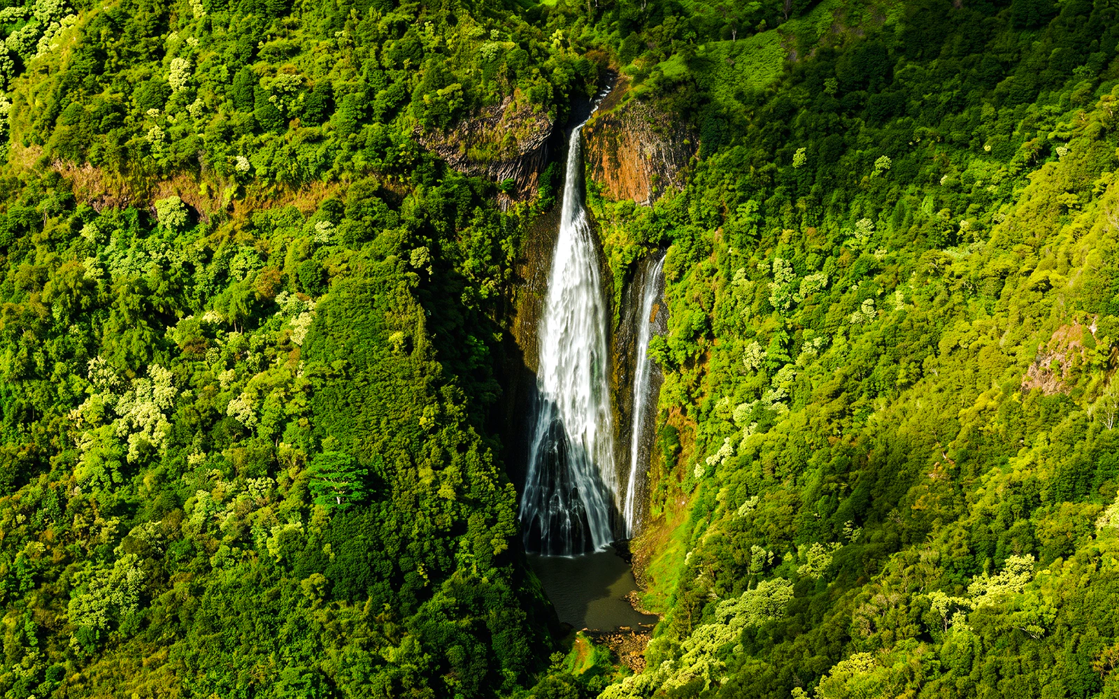 Aerial view of a waterfall surrounded by lush greenery in Kauai, Hawaii.
