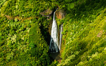 Aerial view of a waterfall surrounded by lush greenery in Kauai, Hawaii.
