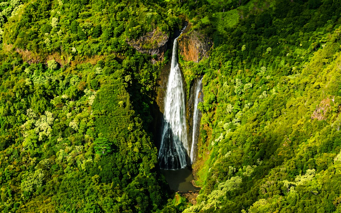 Aerial view of a waterfall surrounded by lush greenery in Kauai, Hawaii.