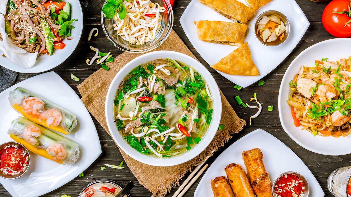 Vietnamese dishes including pho, spring rolls, and noodle salad arranged on a table.