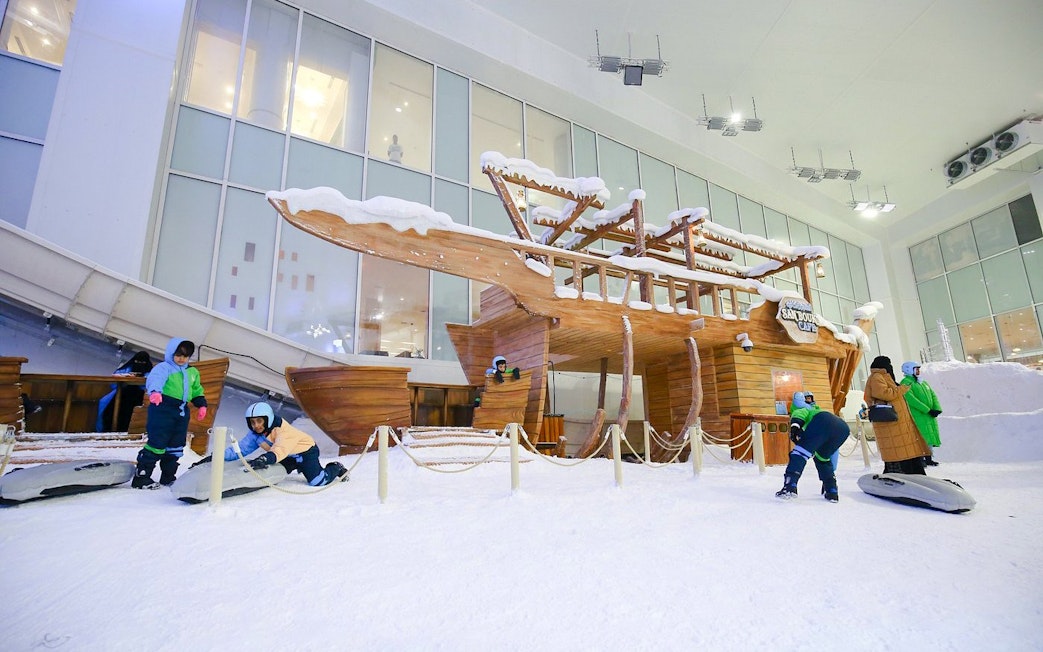 Children playing on sleds near a snow-covered wooden structure at Snow Dunes Theme Park.