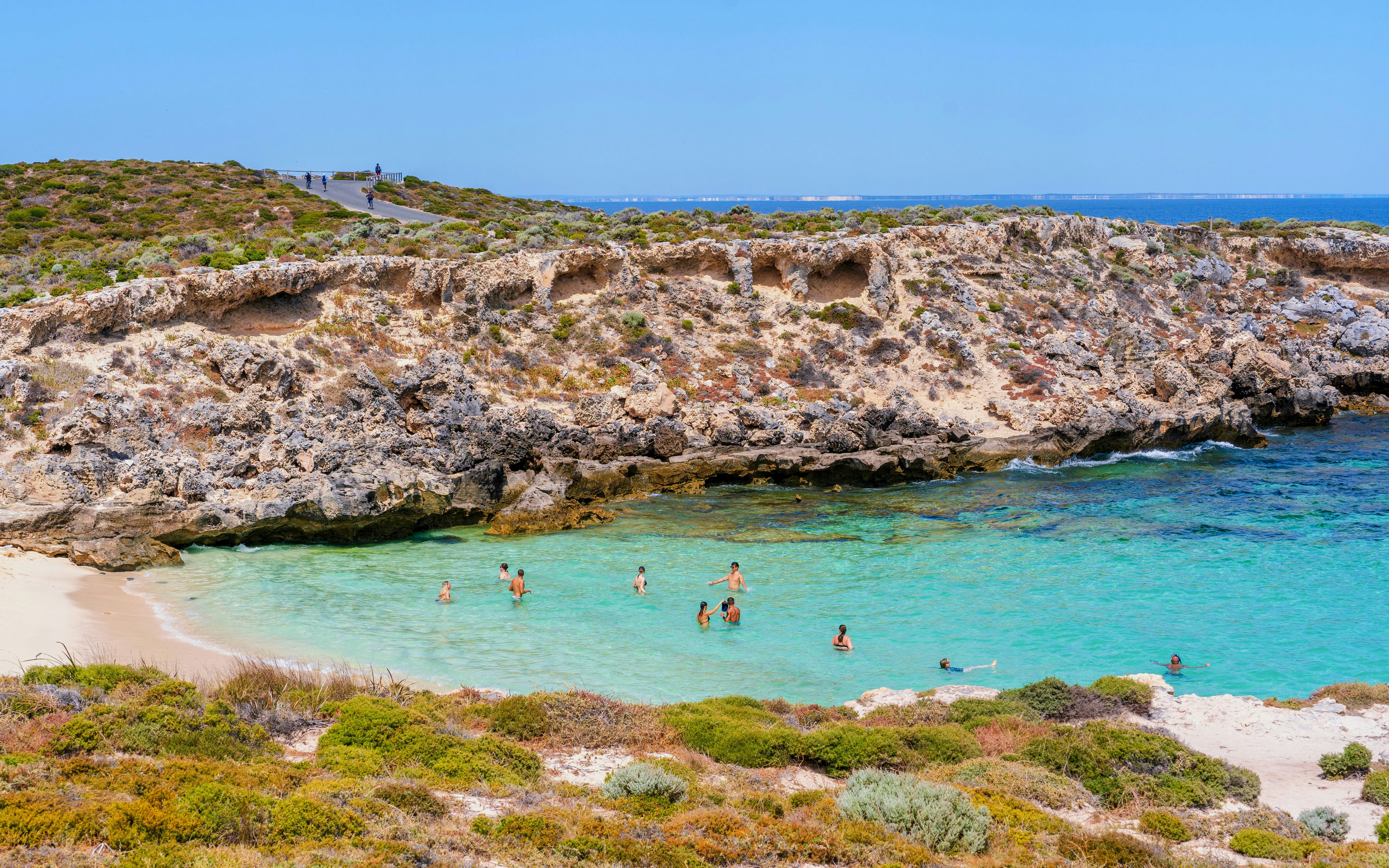 Swimmers enjoying clear waters at Little Salmon Bay, Rottnest Island, with rocky cliffs in the background.