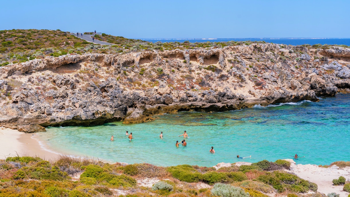 Swimmers enjoying clear waters at Little Salmon Bay, Rottnest Island, with rocky cliffs in the background.
