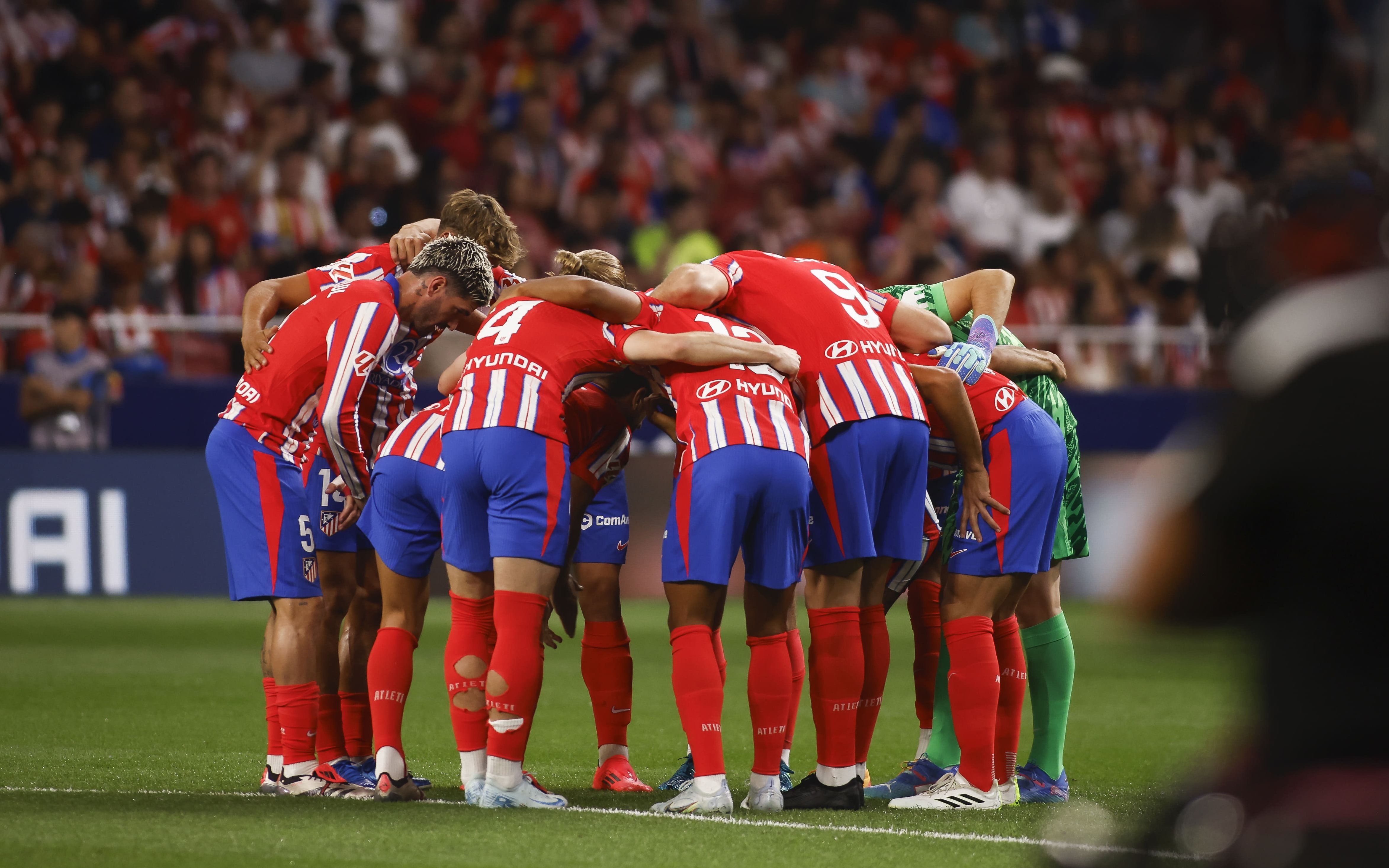 Atlético Madrid players in a team huddle during a match.