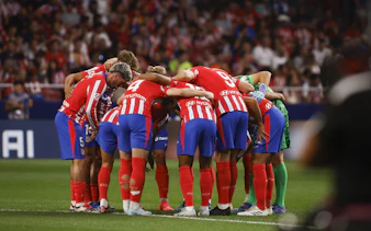 Atlético Madrid players in a team huddle during a match.