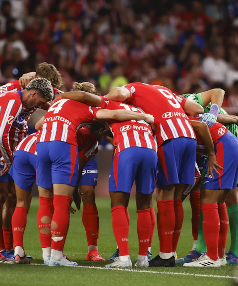 Atlético Madrid players in a team huddle during a match.