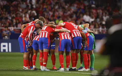 Atlético Madrid players in a team huddle during a match.