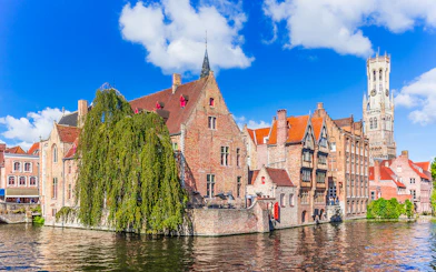 Historic buildings along a canal in Bruges with the Belfry tower in the background.
