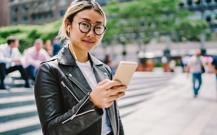 Asian woman using audio guide on smartphone in urban setting.