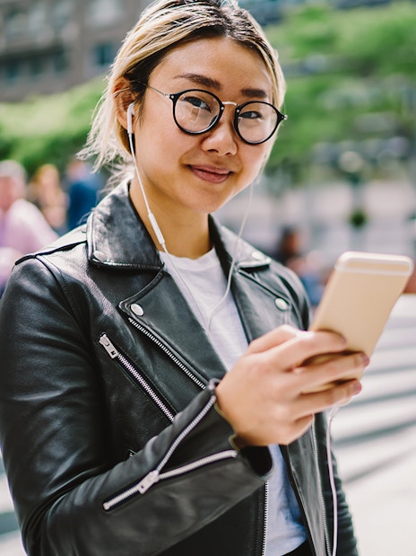 Asian woman using audio guide on smartphone in urban setting.