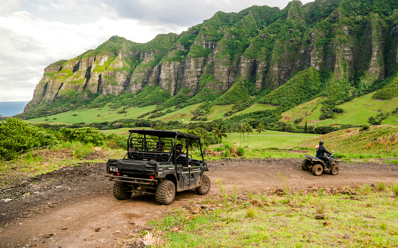UTVs driving on a dirt trail at Kualoa Ranch, Oahu, Hawaii, with lush green mountains in the background.