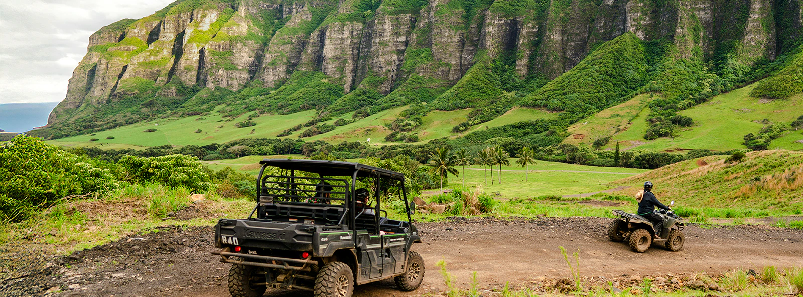UTVs driving on a dirt trail at Kualoa Ranch, Oahu, Hawaii, with lush green mountains in the background.