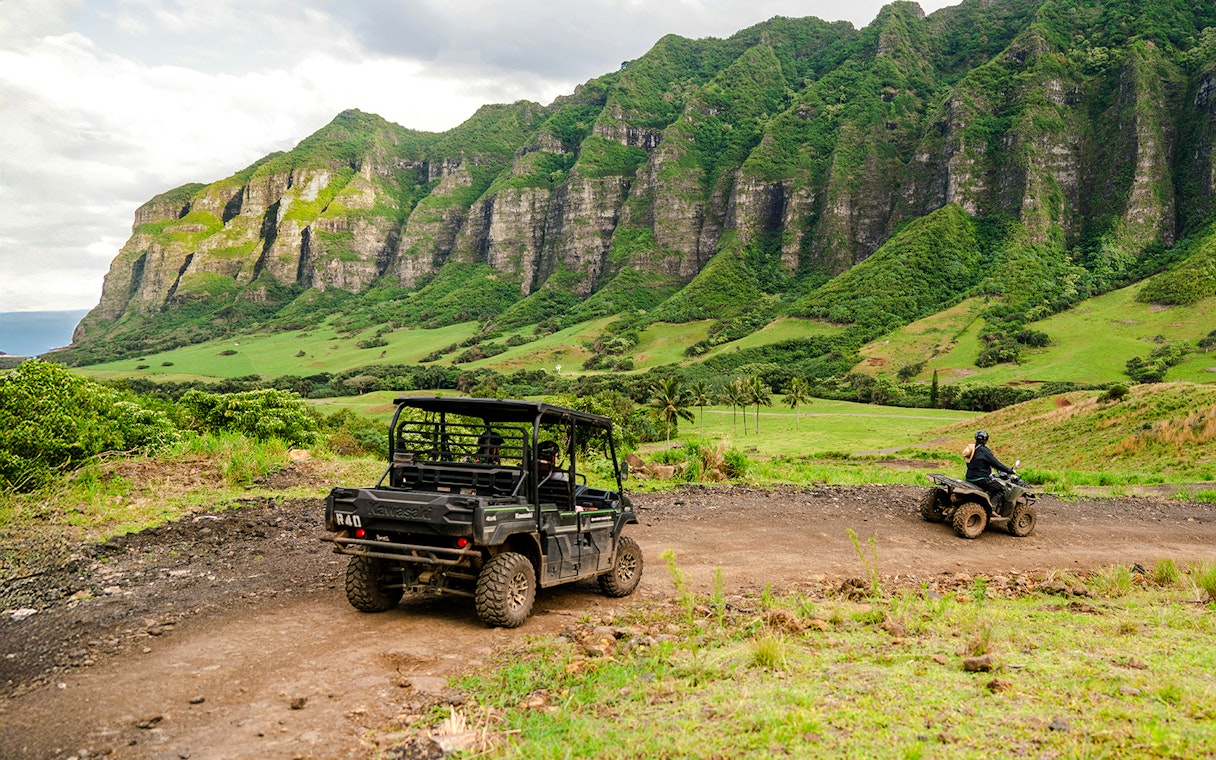 UTVs driving on a dirt trail at Kualoa Ranch, Oahu, Hawaii, with lush green mountains in the background.