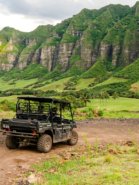UTVs driving on a dirt trail at Kualoa Ranch, Oahu, Hawaii, with lush green mountains in the background.
