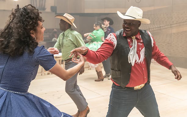 Dancers in cowboy attire performing a lively routine for the musical Oklahoma!