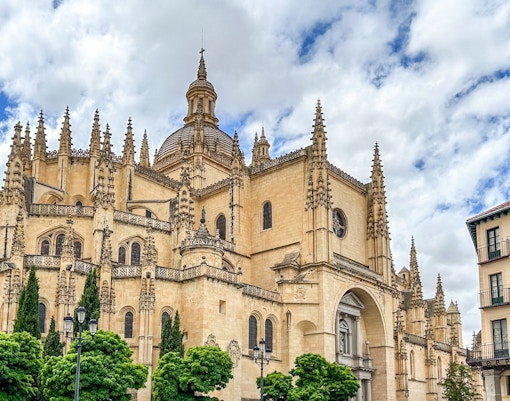 Segovia Cathedral with Gothic spires and detailed facade under a cloudy sky.