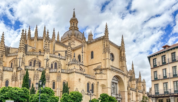 Segovia Cathedral with Gothic spires and detailed facade under a cloudy sky.