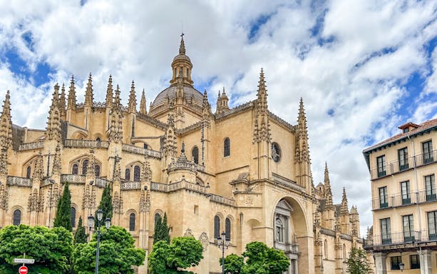 Segovia Cathedral with Gothic spires and detailed facade under a cloudy sky.