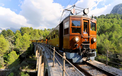 Vintage train crossing a bridge in Mallorca's scenic landscape.