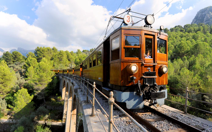 Vintage train crossing a bridge in Mallorca's scenic landscape.