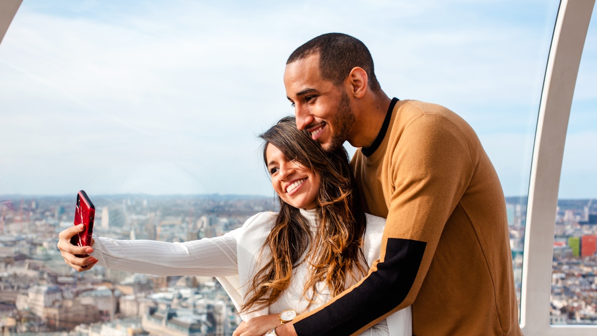 Couple taking a selfie on the London Eye with cityscape view.