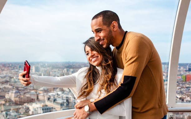 Couple taking a selfie on the London Eye with cityscape view.
