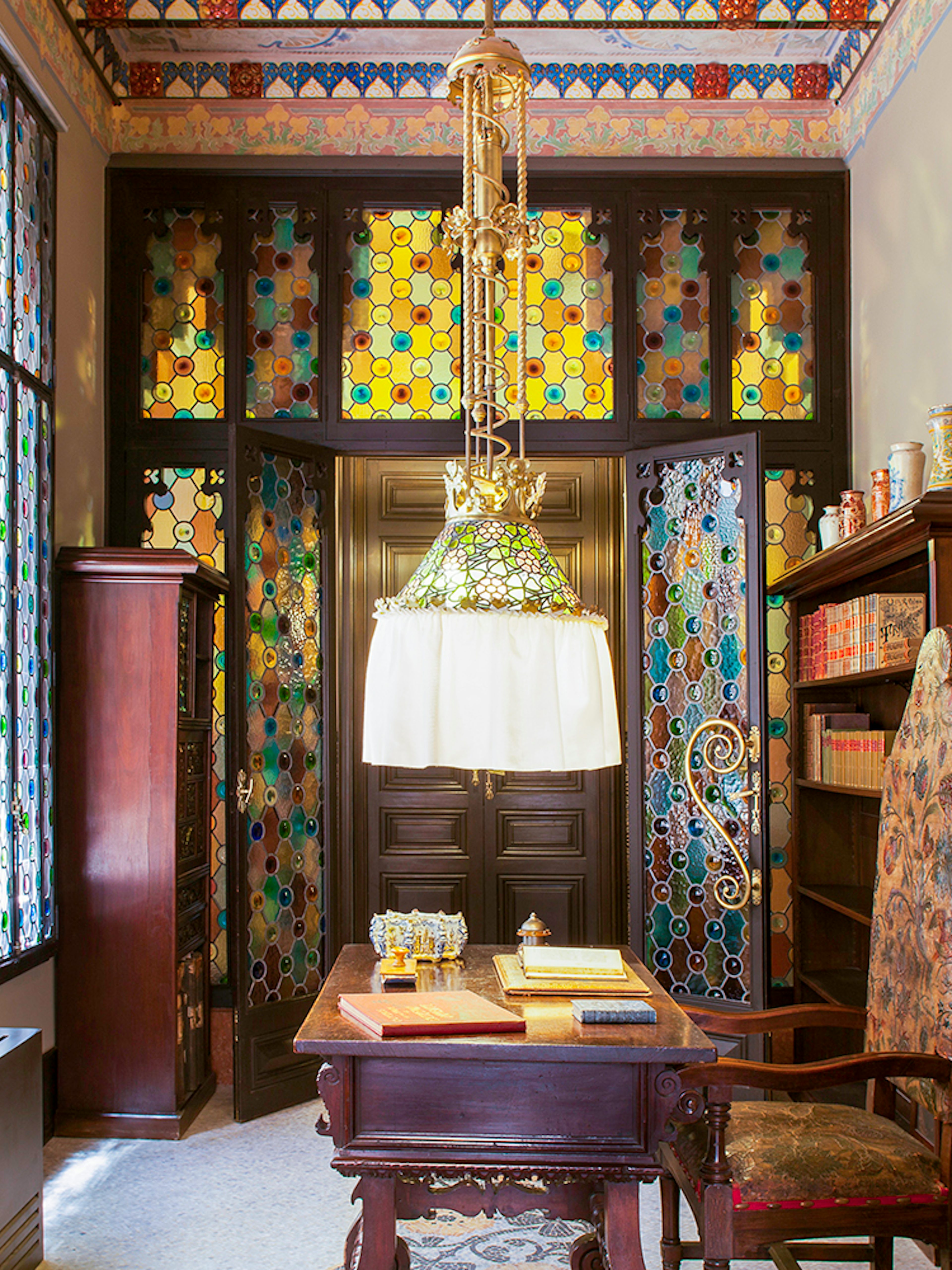 Stained glass interior of Casa Amatller with ornate wooden furniture and colorful windows.