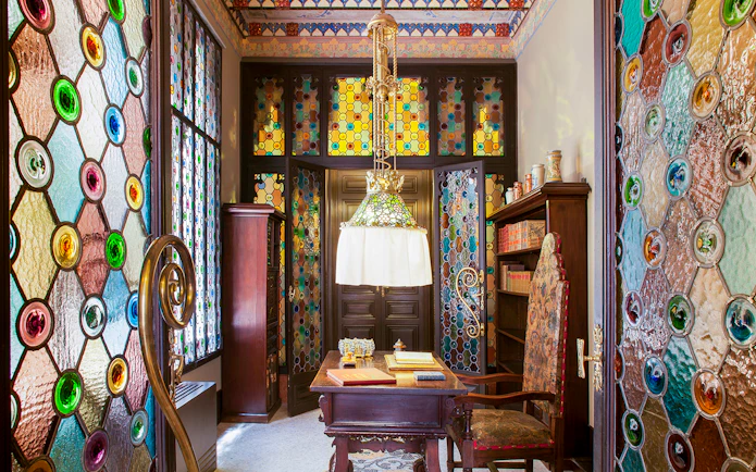 Stained glass interior of Casa Amatller with ornate wooden furniture and colorful windows.