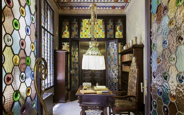 Stained glass interior of Casa Amatller with ornate wooden furniture and colorful windows.