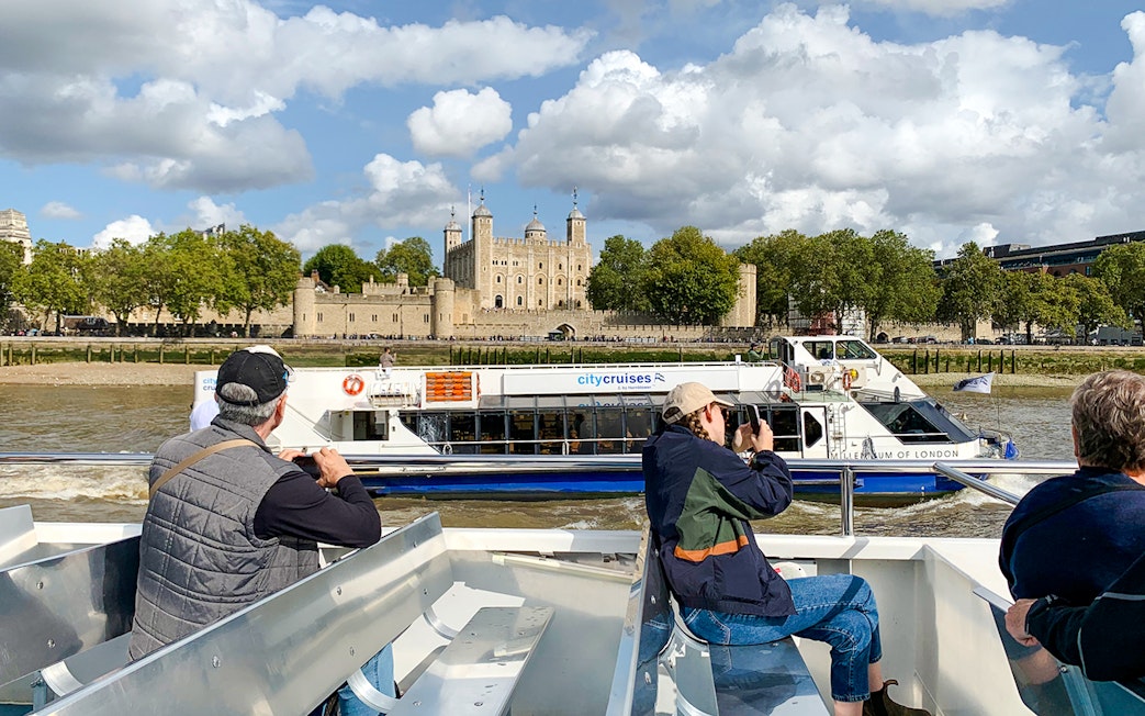 Sightseeing cruise passengers view the Tower of London from the Thames River.