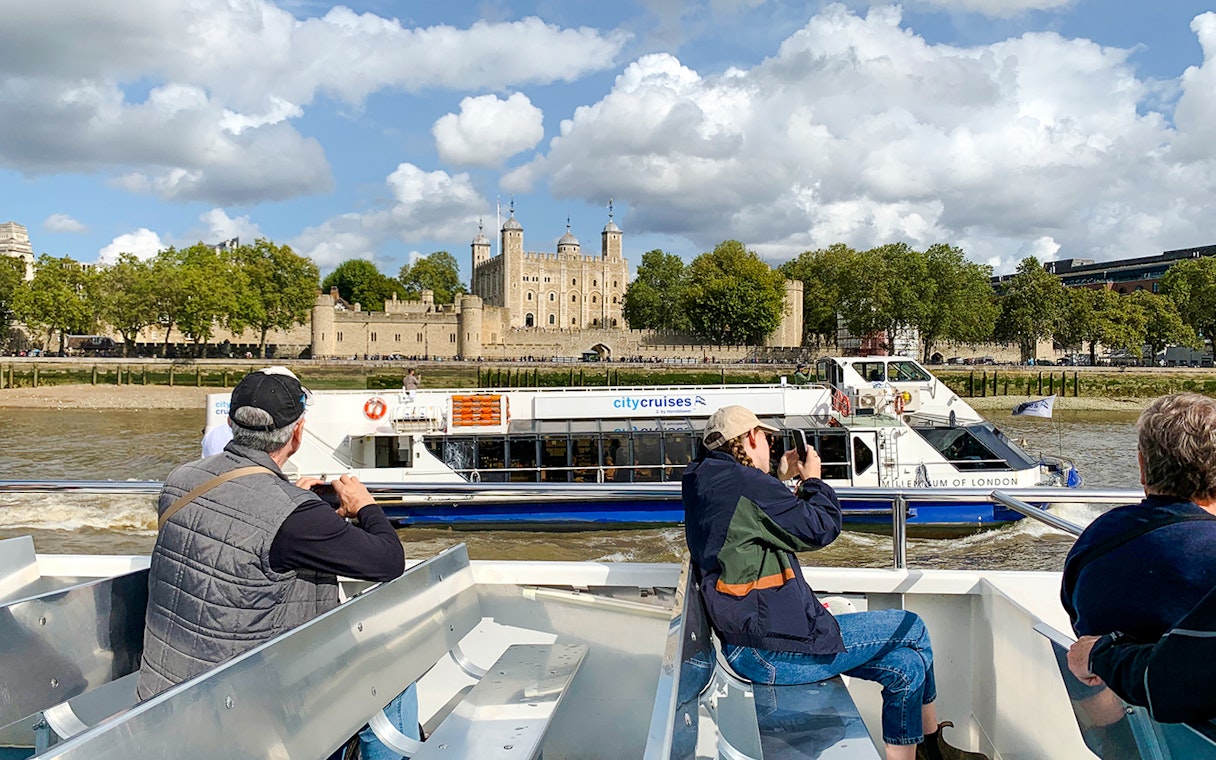 Sightseeing cruise passengers view the Tower of London from the Thames River.
